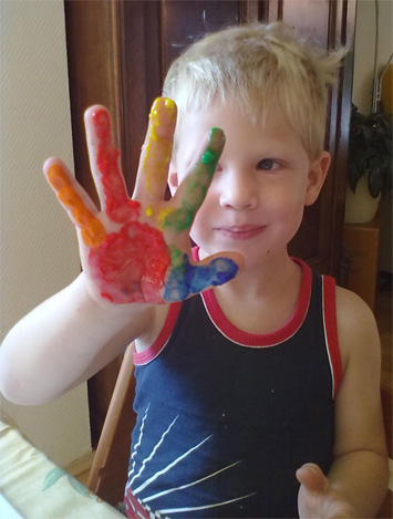 Ein Kind hÃ¤lt eine Hand hoch, die mit Fingerfarben bunt angemalt wurde